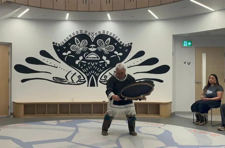 A man dressed plays a drum in a indoor setting